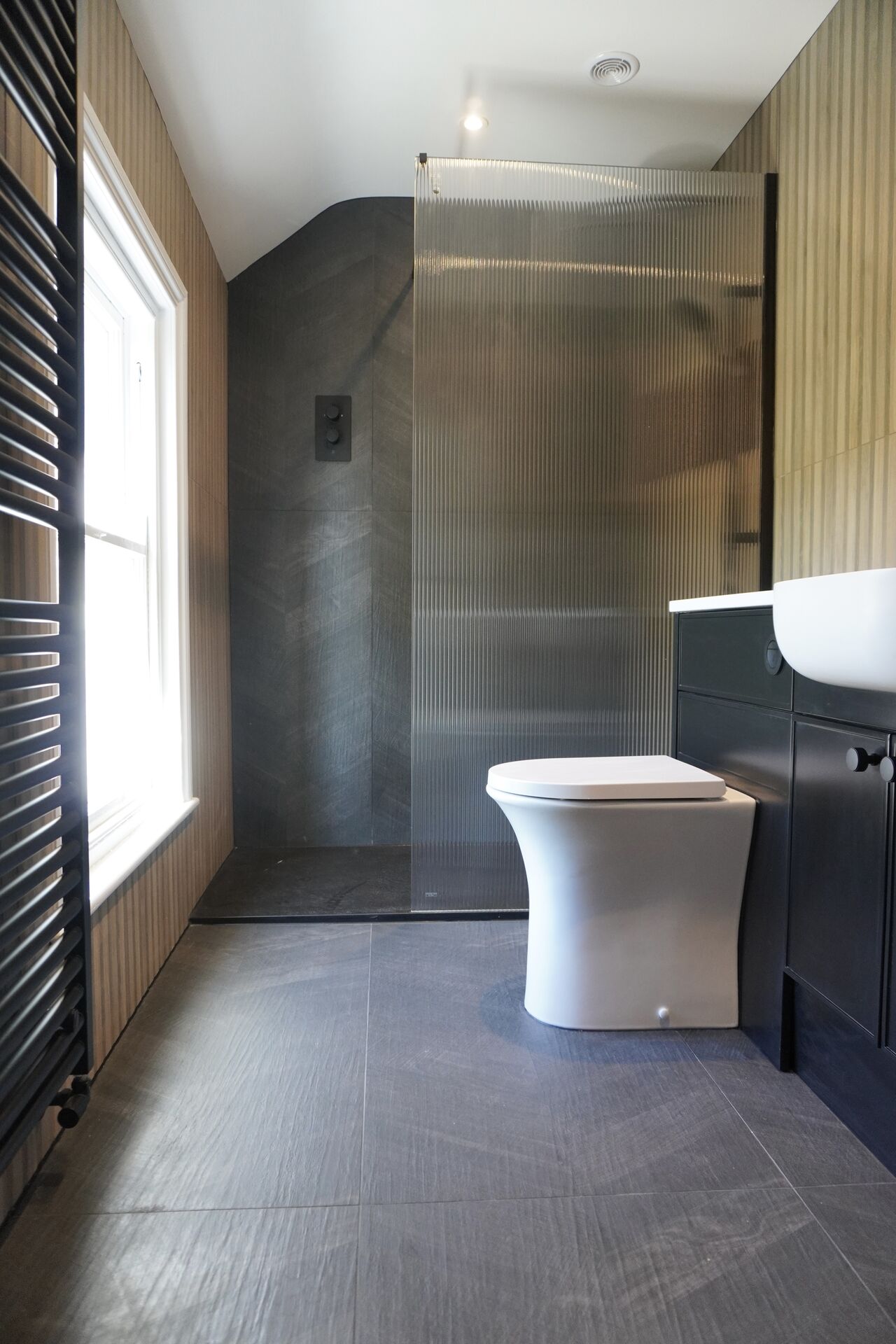 Fluted glass shower screen beside a wall-hung toilet