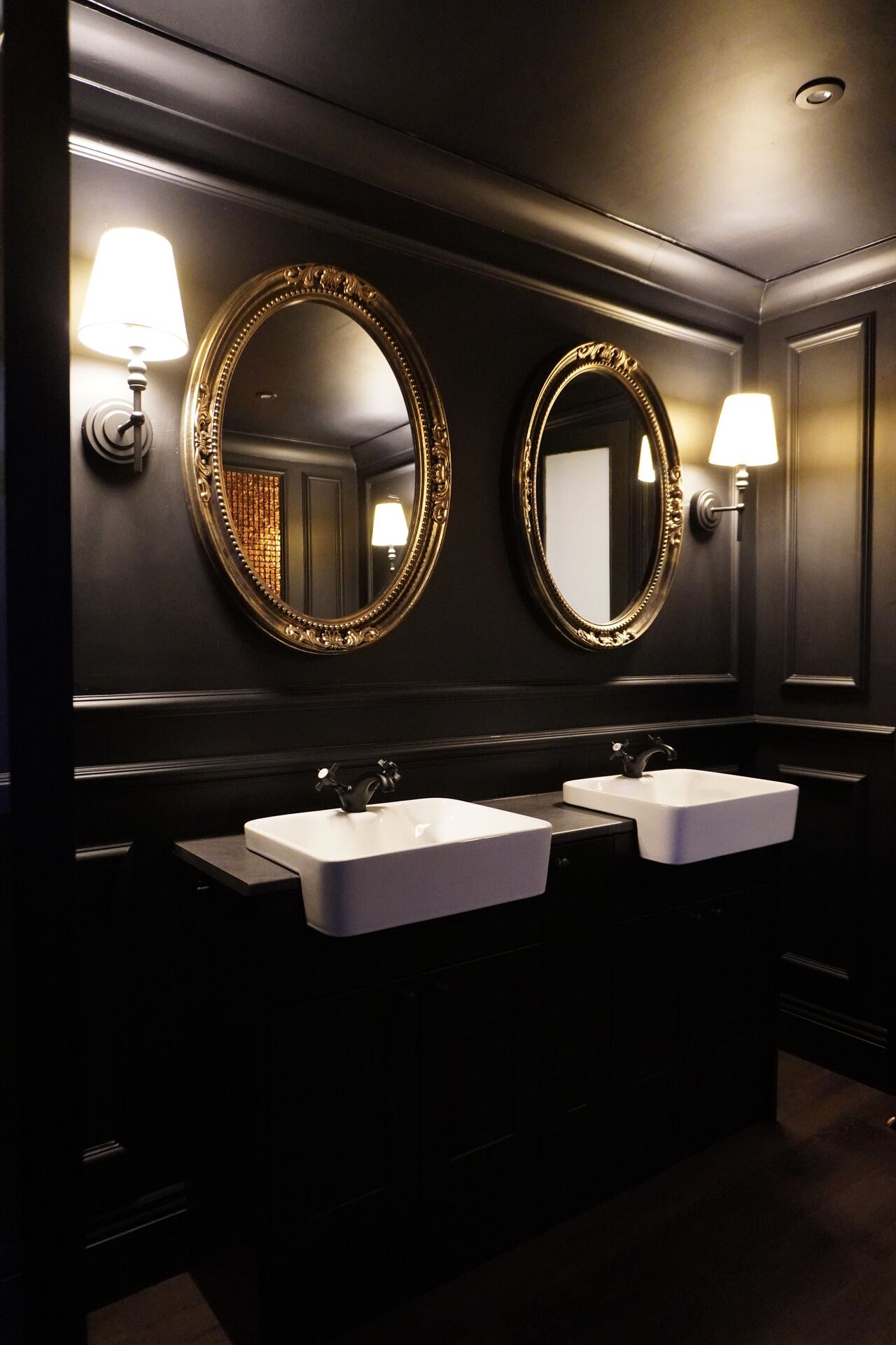 Dark, moody powder room with twin oval mirrors