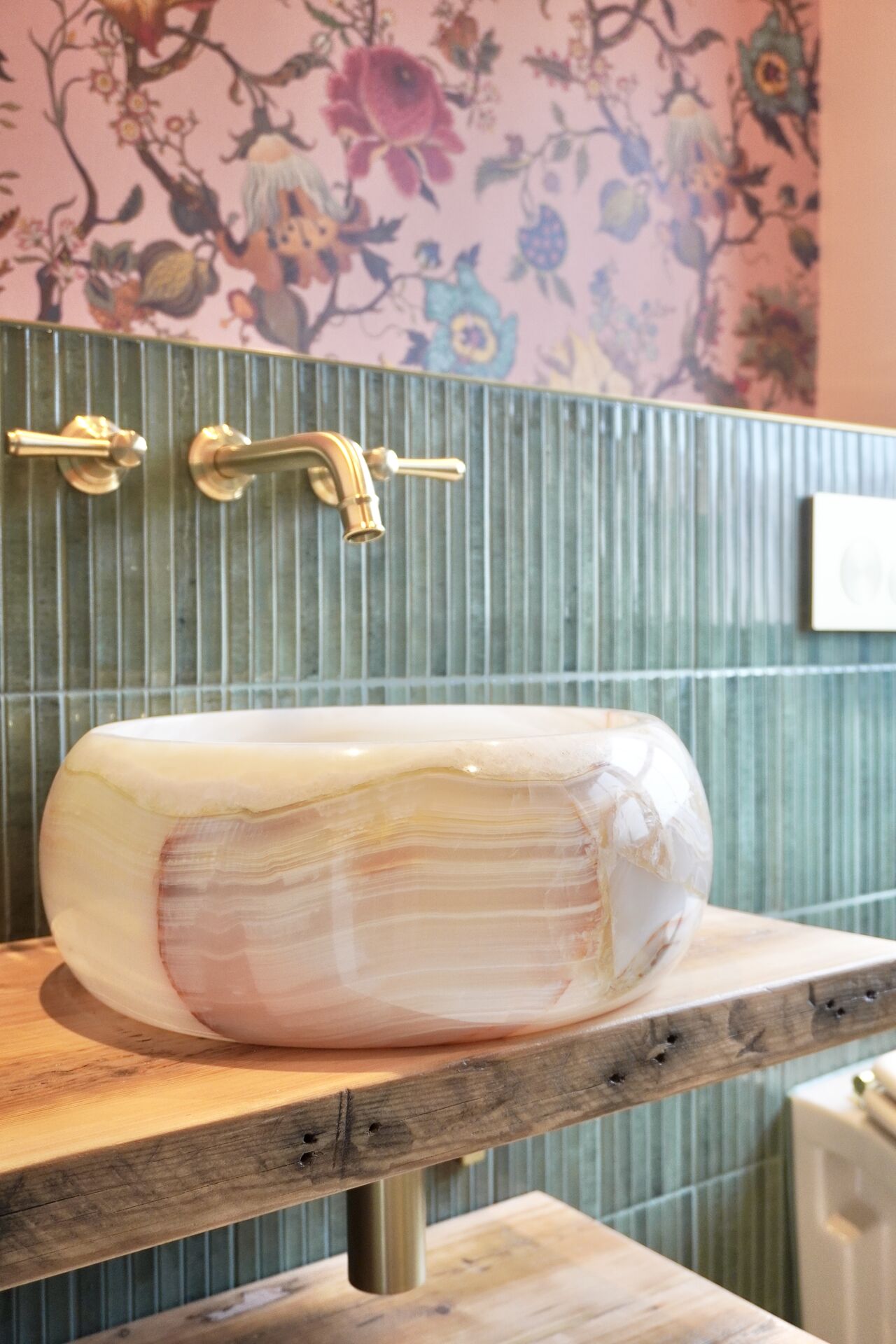 Onyx vessel basin against patterned wallpaper and ribbed green tile
